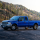 A blue truck parked on pavement in the mountains during magic hour.